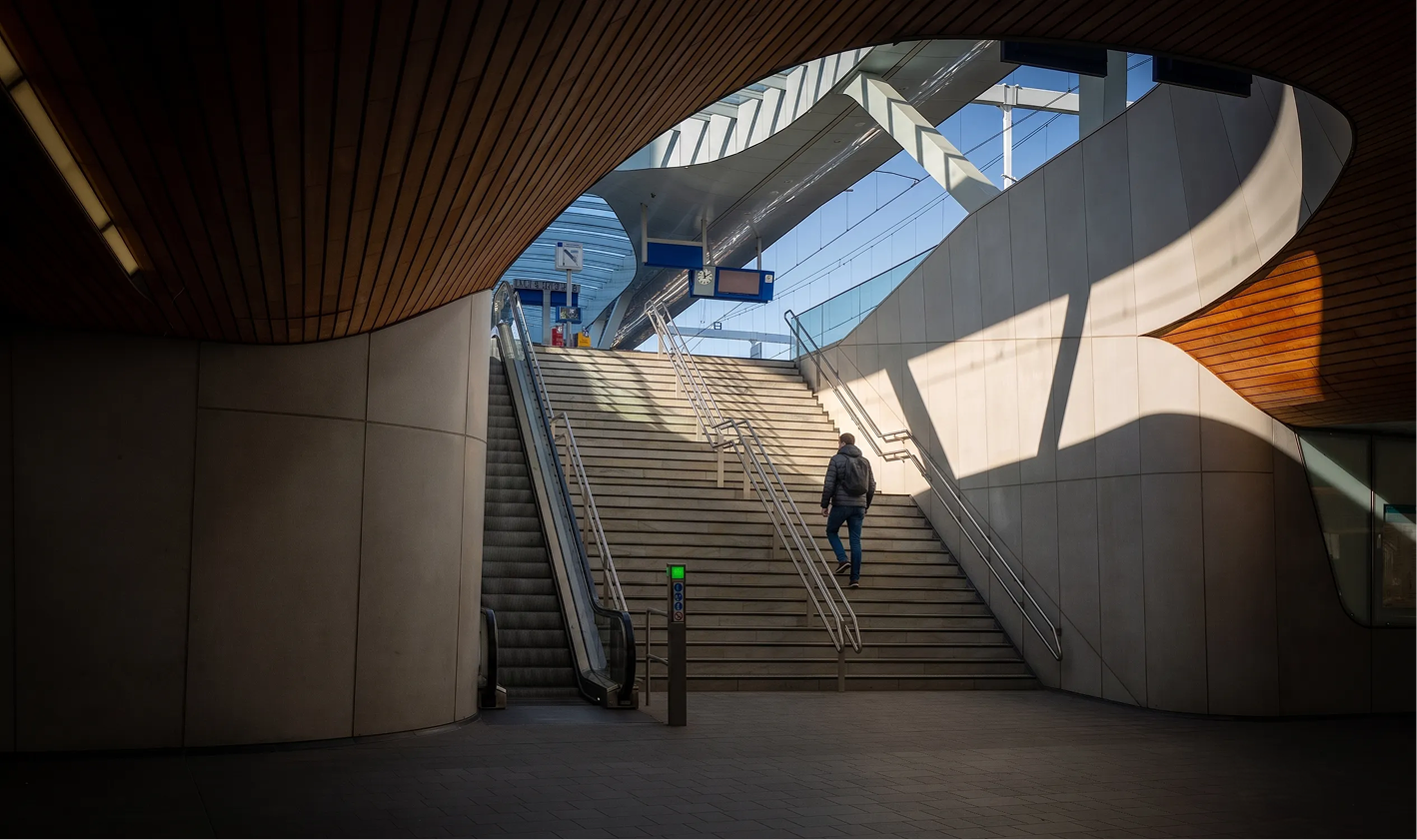 Person walking up curved concrete stairs beneath a modern wooden ceiling structure.
