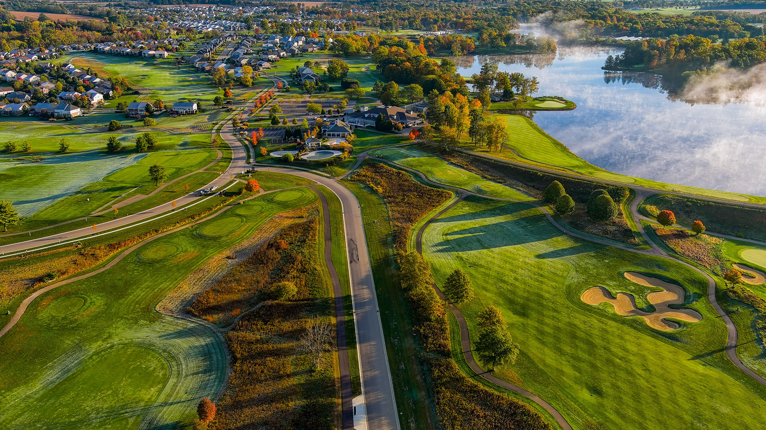 Aerial view of golf course, road, and lakeside town in autumn.