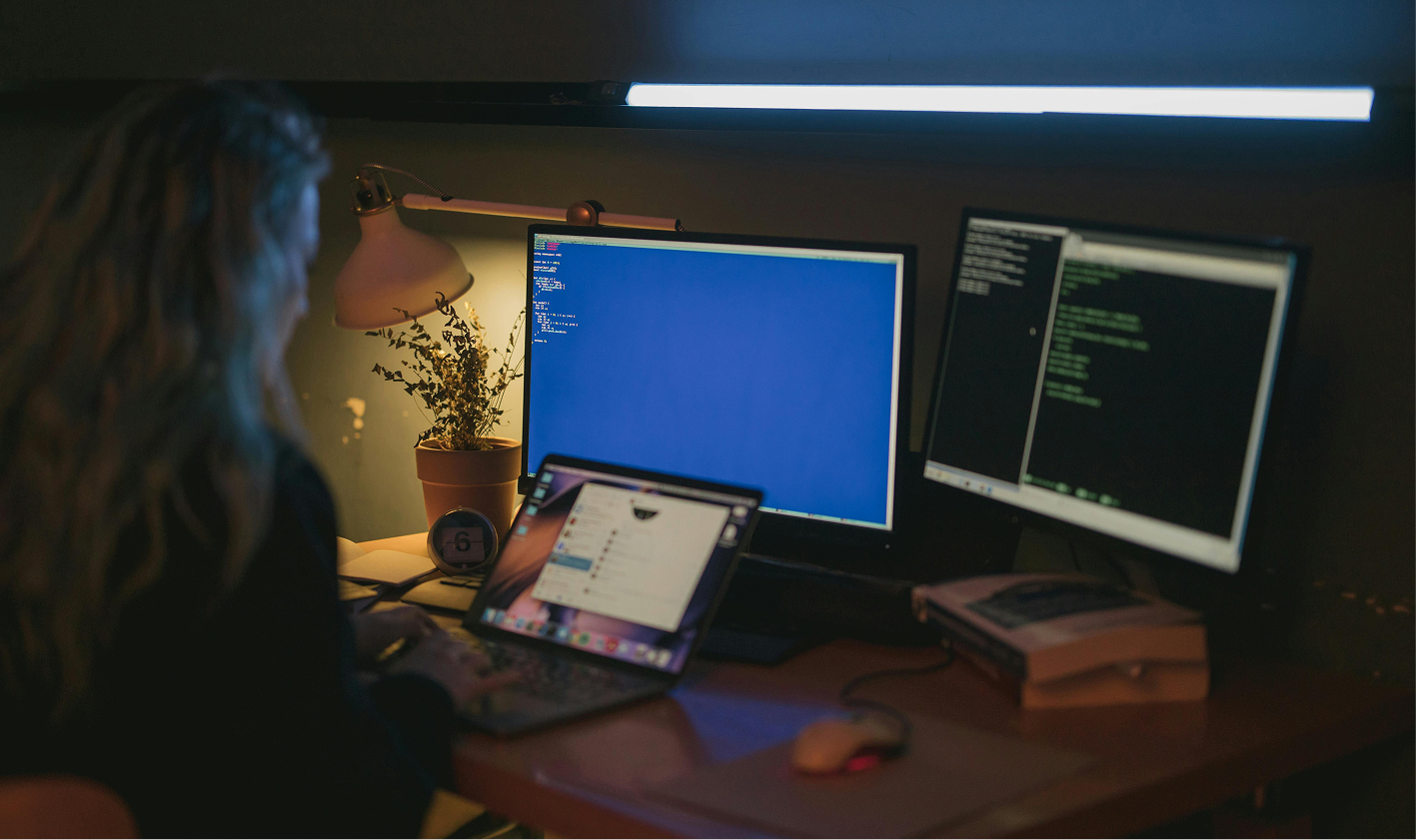 Person at desk with blue error screen and code editor on dual monitors.