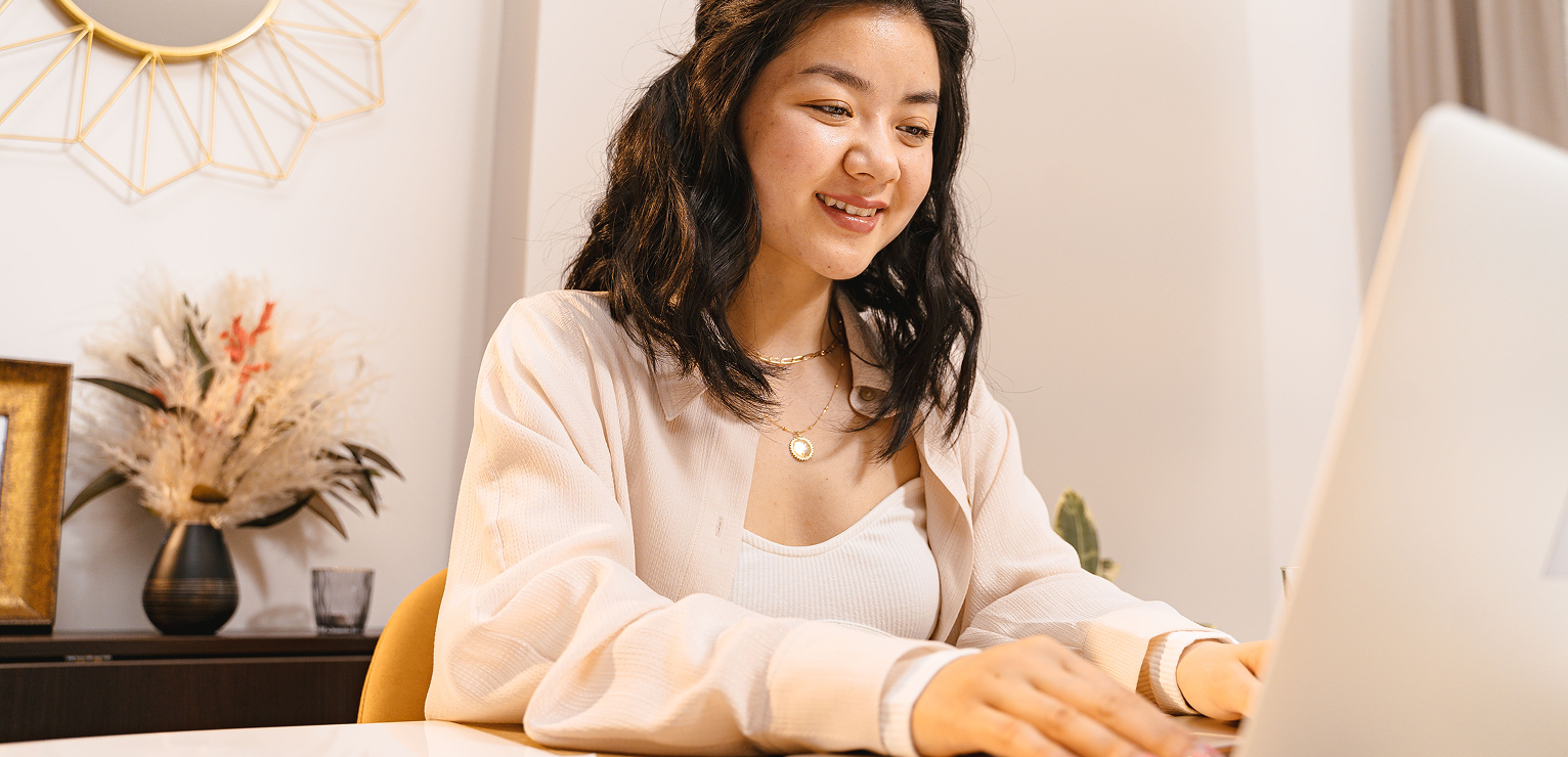 Smiling woman using a laptop at a home desk, photograph.