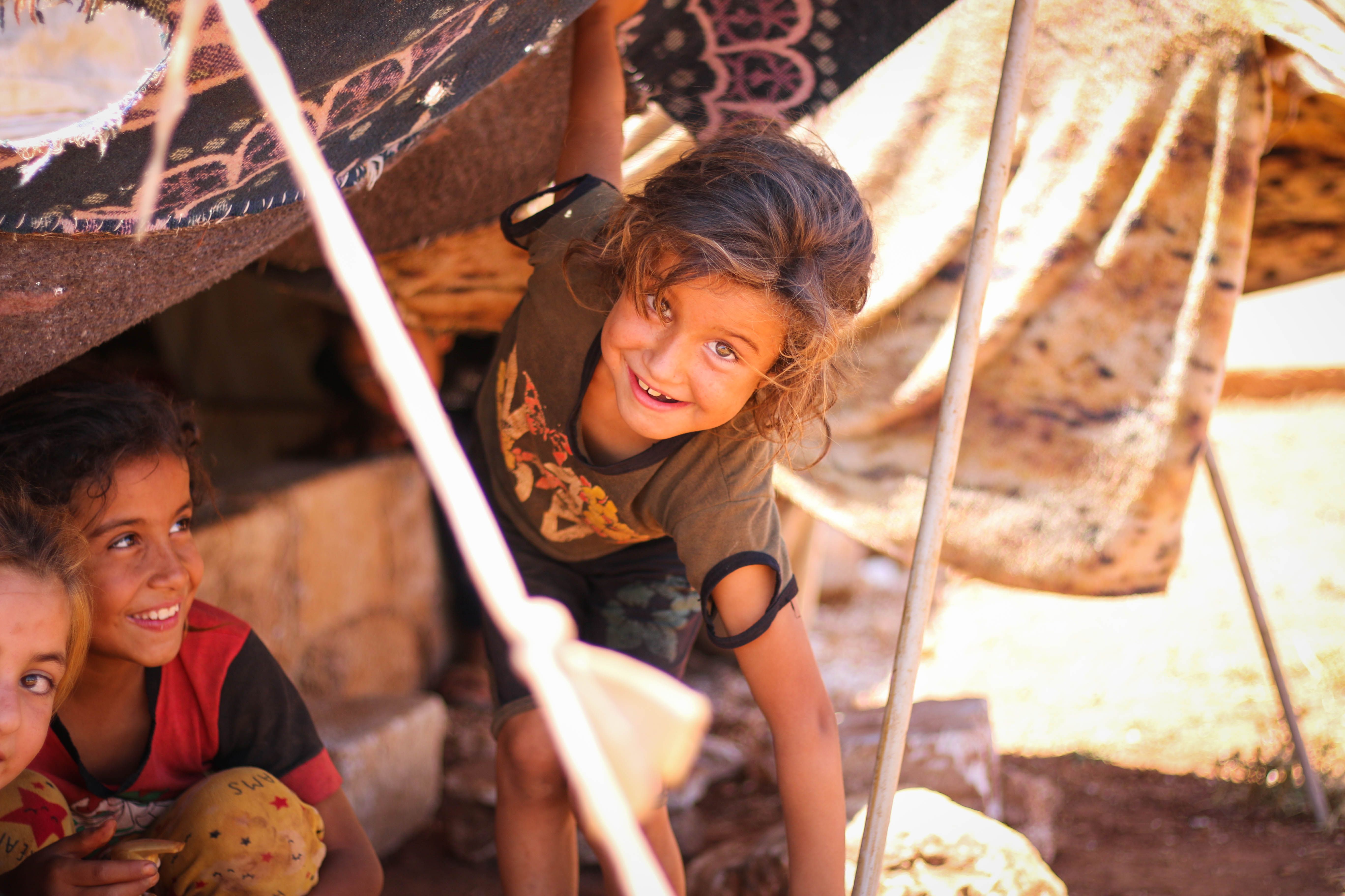Children playing inside a fabric tent, one smiling and peeking through the opening.