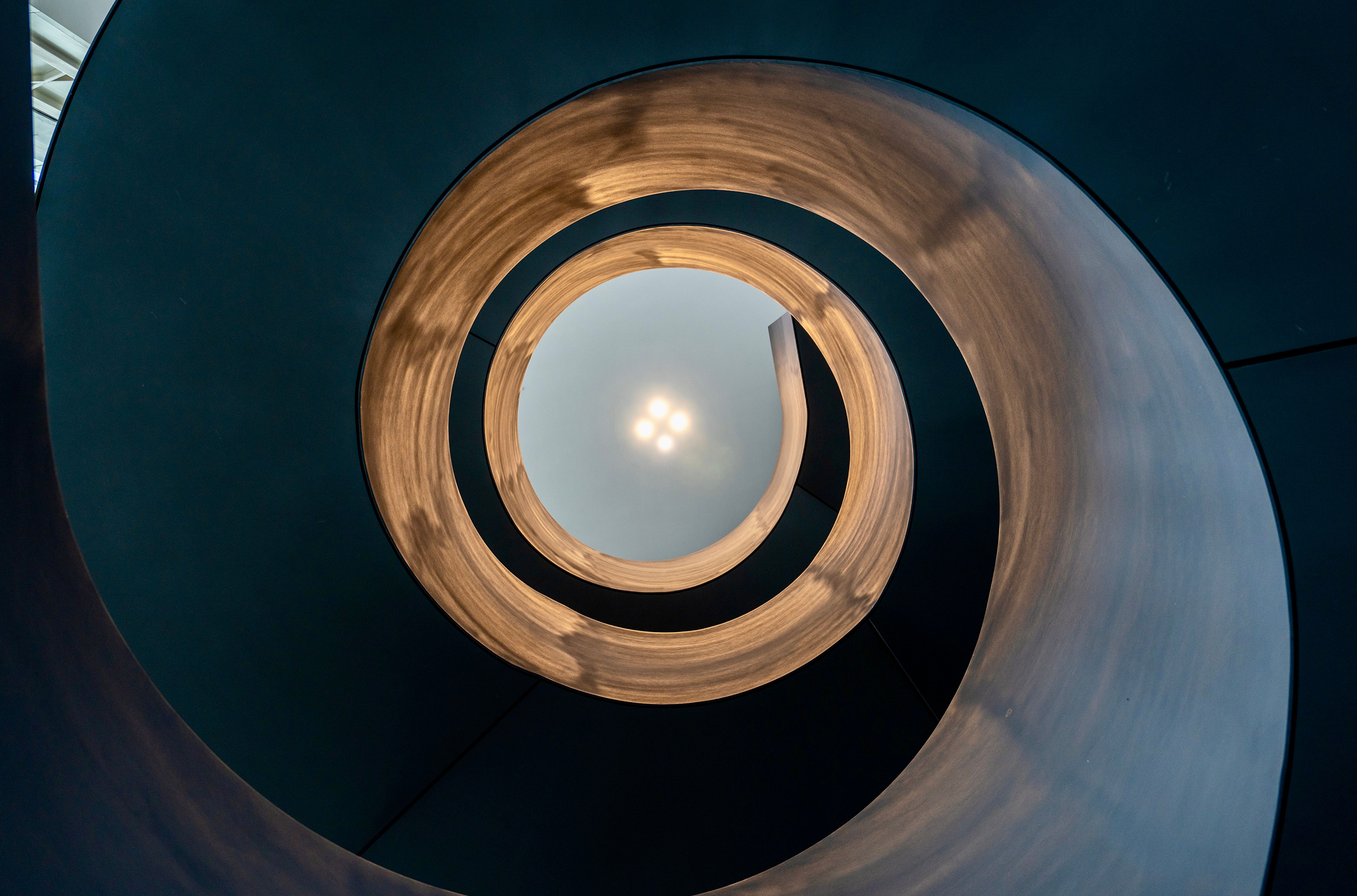 Spiral staircase viewed from below, forming a swirling circular pattern with light at center.
