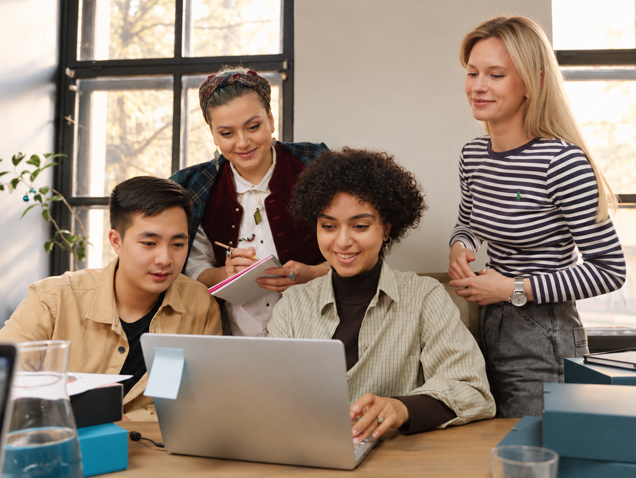 Four colleagues collaborating around a laptop in a bright office setting.