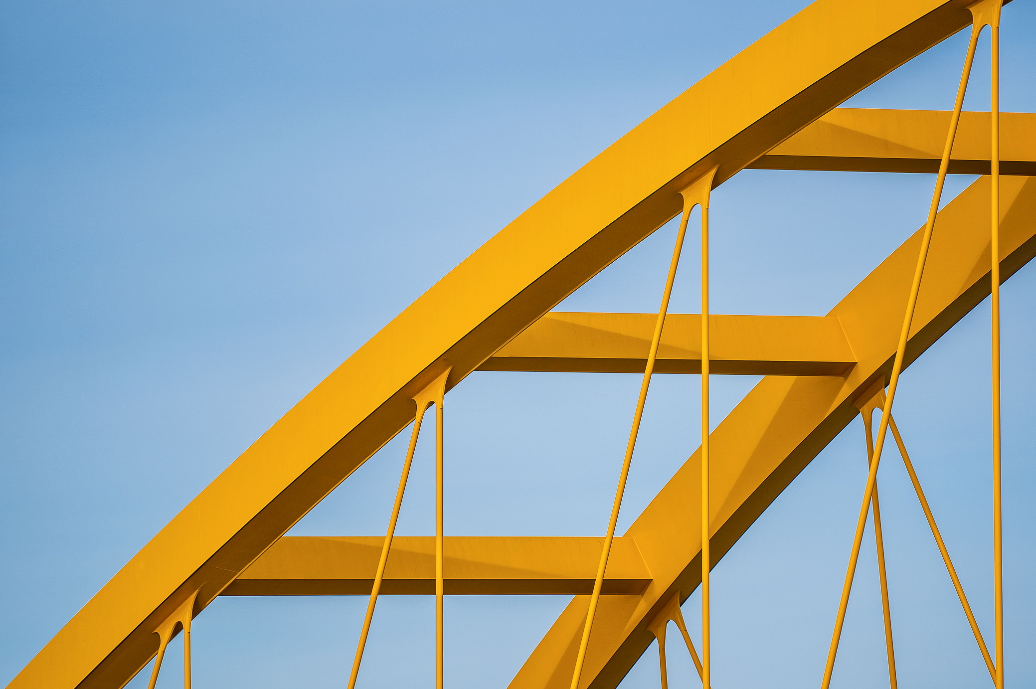 Yellow arch bridge structure with cable supports against a blue sky.