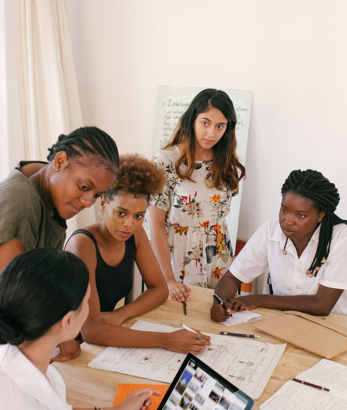 Group of women collaborating around a table with papers and a laptop, photograph.