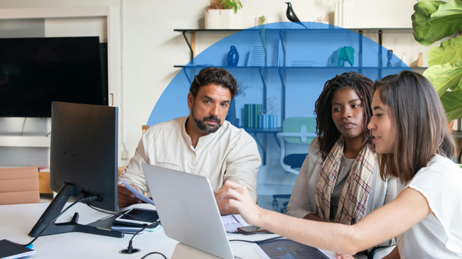 Three people working on a laptop in an office